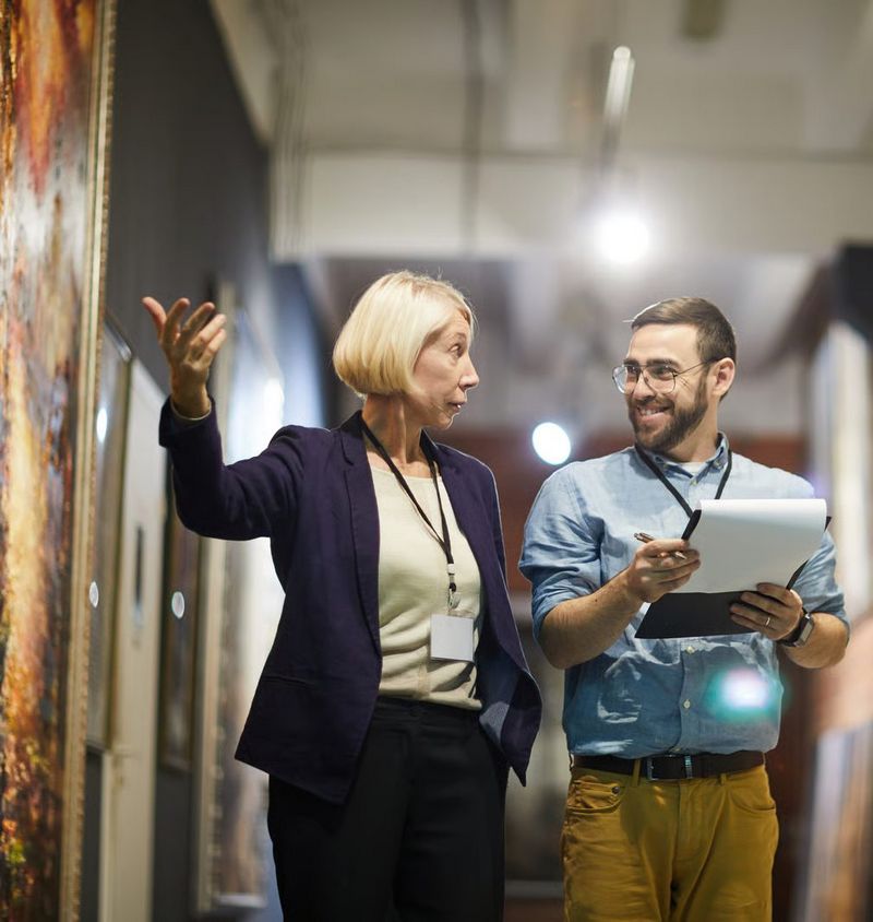 Zdjęcie przedstawiające dwie osoby, kobietę i mężczyznę stojących przy ścianie wypełnionej obrazami